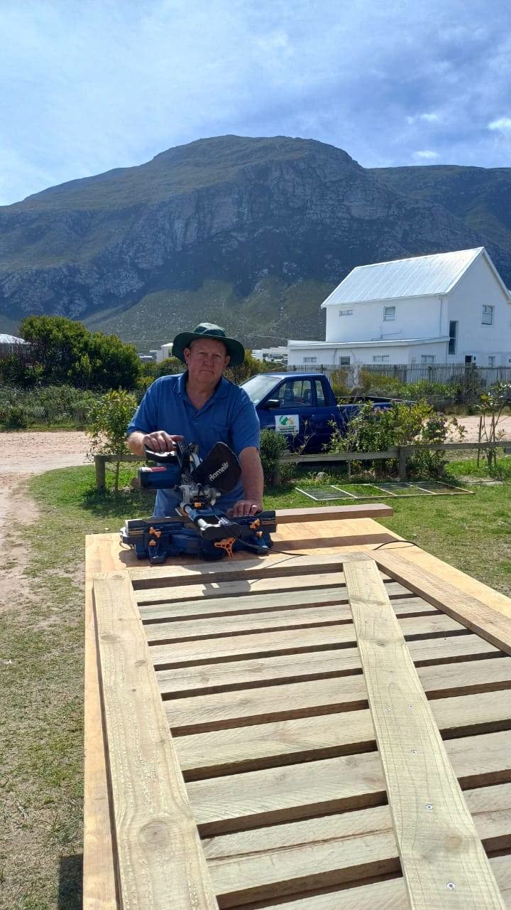 Neville Banwell cutting timber with a mitre saw in front of the mountain at Betty's Bay
